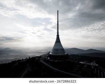 At Jested Mountain Hotel in Liberec, a modern architectural marvel stands against a cloudy sky during sunset. The evening light casts a beautiful glow over the landscape, creating a serene atmosphere.
