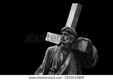 Jesus Christ with cross.  Ancient statue isolated on black background. 
