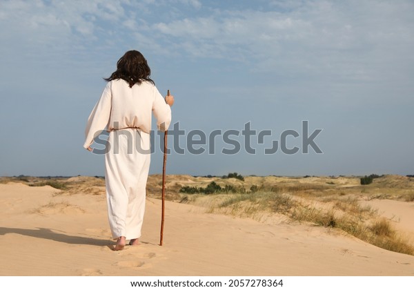 Jesus Christ walking with stick in desert, back\
view. Space for text