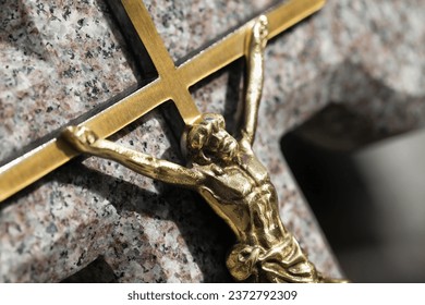 Jesus crucified golden metal statue. Weathered granite cross. Graveyard background. Shiny gold symbol. All saints day. Old abandoned tombstone. Cemetery grave. Catholic religion symbol.