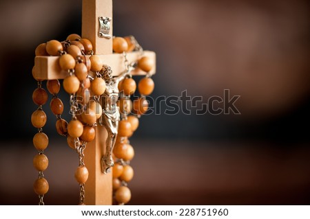 Jesus figurine and rosary made of wood beads dangle on wooden cross, INRI sign above, horizontal orientation, nobody.