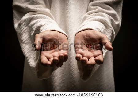 Jesus of Nazareth showing the wounds on his hands while praying on a dark night after being resurrected.