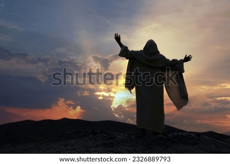 Jesus praying alone with raised hands on a hill at sunset. Biblical concept.
