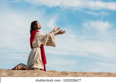 Jesus Praying On Knees On Sand In Desert Against Sky 