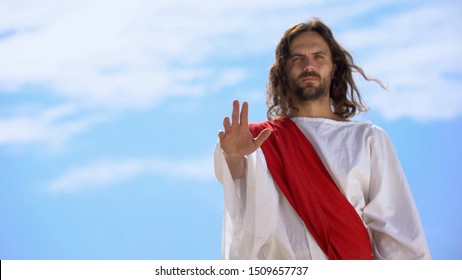 Jesus in robe stretching opened palm on camera, blessing and healing, template