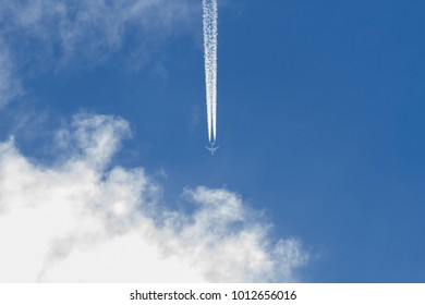 Jet Airplane Flying In The Blue Sky With Clouds. Wake Leaving Trace Or Steam Jet, Viewed From Below 