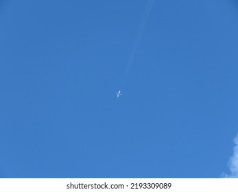 Jet Airplane Flying Overhead In Bright Blue Sky Edged By Fluffy White Cloud