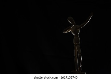 Jet black background with a wooden model mannequin in a dab pose, backlit  - Powered by Shutterstock