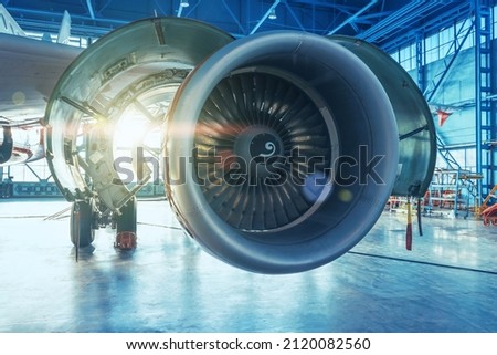 Jet engine with open hood covers on maintenance, illuminated by bright light from behind the hangar gate