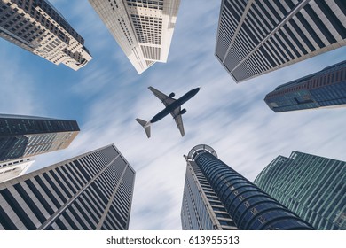 Jet Plane Aircraft Traveling In The Sky Over City Buildings In Downtown Travel Destination Of Singapore City. Showing Concept Of Tourism Transportation, Airplane Manufacturing And Airline Business.