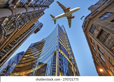 A jet plane flying low over Three different kind of architecture with commercial office buildings exterior. Evening view at bottom skyscrapers.