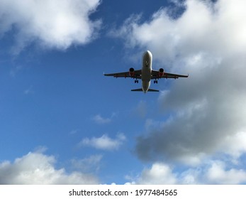 Jet Plane Overhead In Blue Sky, Taking Off From Airport. White Fluffy Clouds