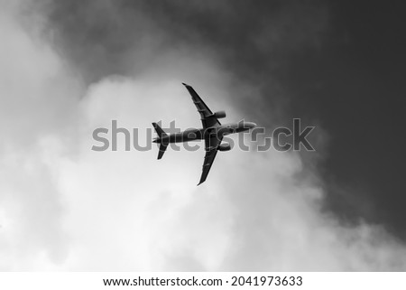 Jet plane taking off with blue sky and white cloud. Black and white greyscale of modern passenger air plane with two turbine engines seen from below after lifting off in Westerland Sylt Germany.