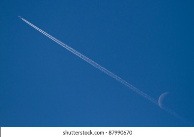 Jet Stream Of Airplane Going Through The Moon In Blue Sky