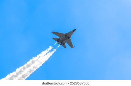 Jet with Vapor Trails in Sky: A military jet soars through a bright blue sky, leaving white vapor trails behind. The perspective captures the aircraft flying overhead in dynamic motion. - Powered by Shutterstock