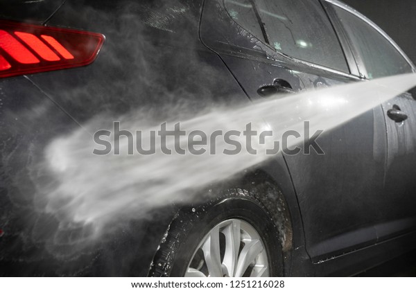 A jet of water knocks dirt from a car under high\
pressure. Car wash