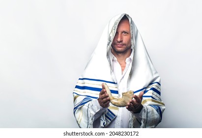 Jew man wrapped in a Tallit, prayer shawl holding the Shofar (horn). Rosh hashanah (Jewish New Year), Shabbat and Yom kippur concept. A rabbi giving a shofar in his hand, before the Tishrei holidays