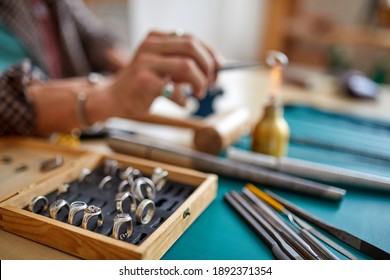 jeweler in the background using flame torch to solder a ring, making durable jewelry. in workshop. focus on rings - Powered by Shutterstock