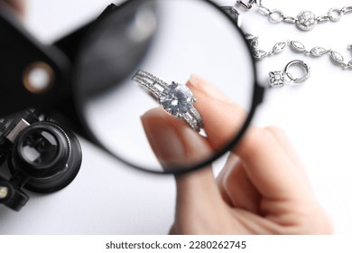 Jeweler examining diamond ring with magnifying glass at white table, closeup - Powered by Shutterstock