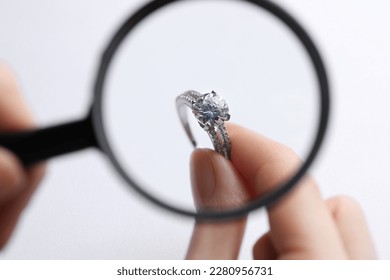 Jeweler examining diamond ring with magnifying glass at white background, closeup - Powered by Shutterstock