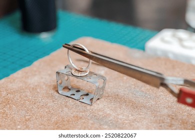 Jeweler holding a ring above metal mold with tweezers while heating with torch. Workplace of jeweler. - Powered by Shutterstock