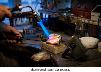 Jeweler Melts With A Flame Silver Or Gold On Old Workbench In Jewelers Workshop