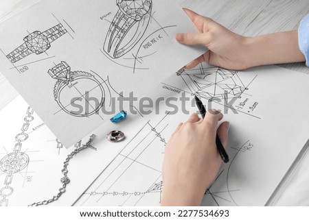 Jeweler with sketches of elegant jewelry at white wooden table, closeup
