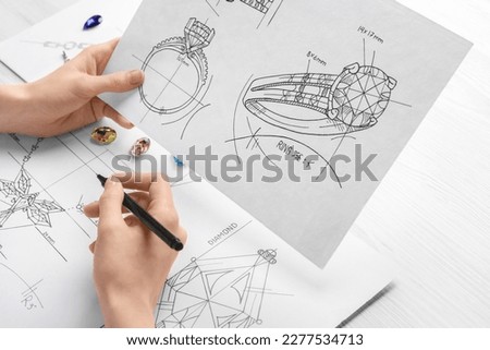 Jeweler with sketches of elegant jewelry at white wooden table, closeup