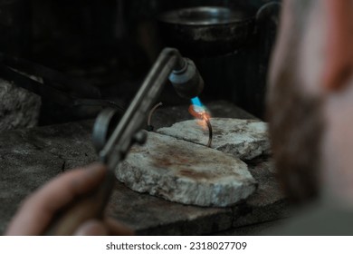 Jeweler soldering on work bench a gold ring bracelet with flame from welding torch in an authentic jewelry workshop - Powered by Shutterstock