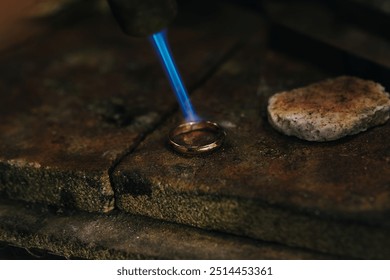 Jeweler soldering on work bench a gold ring with flame from welding torch in an authentic jewelry workshop - Powered by Shutterstock