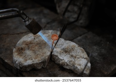 Jeweler soldering on work bench a gold ring bracelet with flame from welding torch in an authentic jewelry workshop - Powered by Shutterstock