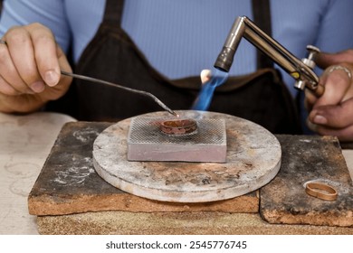 A jeweler uses a blowtorch to solder a metal ring on a heat-resistant surface. This image captures craftsmanship and precision in jewelry-making. Ideal for topics on artisanship, jewelry. - Powered by Shutterstock