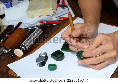A jeweler is using a tool to scrape off the green mold wax.