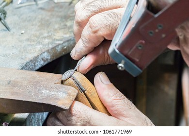 A jeweler wearing a head visor magnifier is engraving diamonds on a ring placed on a wooden clamp with a manual graver.