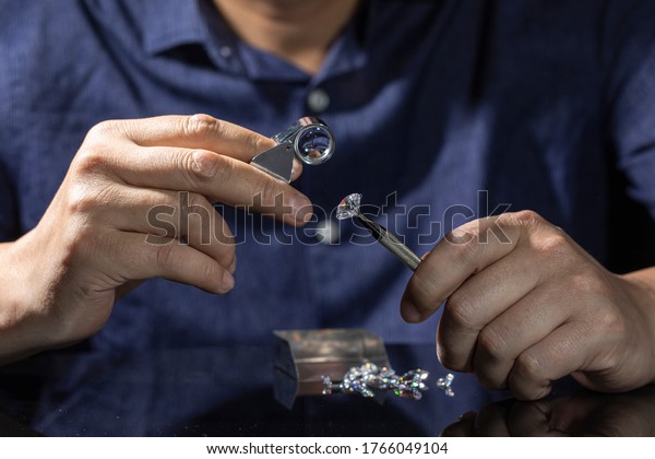 Jeweller examines polish round-cut diamond of\
large size. Close up of jeweller evaluating diamond through\
magnifier. Grading loose brilliant for certification. diamond\
trading business.