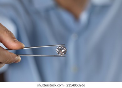 Jeweller holding diamond in tweezers. Closeup of round cut diamond in hand of diamond expert evaluating the quality of gemstone.