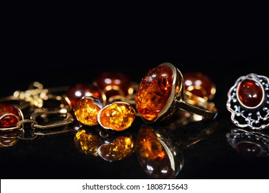 jewelry with amber stones, amber necklace ring and earring and pendant with noble metal like gold, in front of a black background on a black stone with reflection