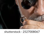 Jewelry appraiser examines a gold ring evaluating large diamond looking through magnifying glass monocular. Professional goldsmith identify gemstones, determine values luxury wedding engagement ring.