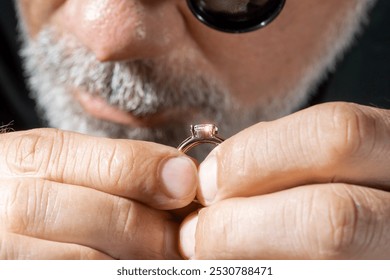 Jewelry appraiser examines a gold ring evaluating large diamond looking through magnifying glass monocular. Professional goldsmith manufacturing or repair luxury wedding engagement ring. - Powered by Shutterstock