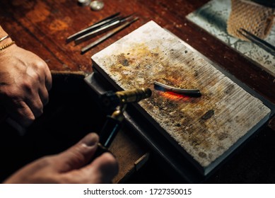 Jewelry artisan heats with a blowtorch a piece of silver that is red-hot in order to make jewelry. jewelry artisan workshop. fire heats the ore. - Powered by Shutterstock