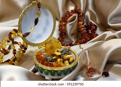 A lot of of jewelry from authentic Baltic amber in ceramic casket,  amber necklace and bracelet on a pastel satin. Gold chain with amber pendant.