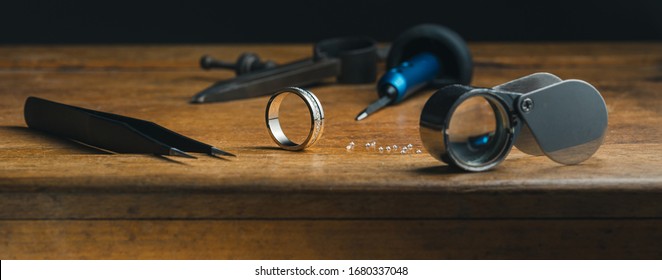 Jewelry Craftsmanship. The Jeweller Engraver Tools And Golden Ring, Diamonds On Wooden Vintage Desk. Side View. Wide CoverTweezers, Magnifier, Chisel Hand Engraving, Diamonds Engagement Golden Ring