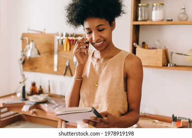 Jewelry designer doing business on phone in ornament studio. Handmade jewelry business owner talking on phone and looking at notebook. - Powered by Shutterstock