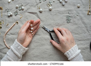 Jewelry designer working in studio with tools making pearl earrings. Close-up of female hands working with jewelry tools
