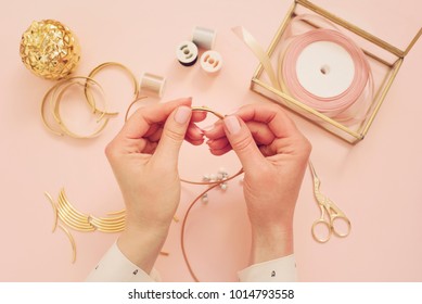 Jewelry designer workplace. Woman hands making handmade jewelry. Freelance fashion femininity workspace in flat lay style. Pastel pink and gold