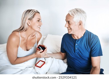 Jewelry, gift and mature couple in bedroom for anniversary, love and romantic gesture in home. Happy woman, man and birthday present with smile for honeymoon, thank you and commitment in marriage - Powered by Shutterstock