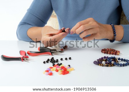 Jewelry making. Production bracelets and necklaces from multi-colored beads. Female hands with a tool on a white. 
Selective focus.
