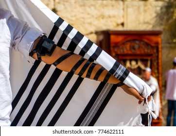 Jewish boy with tefillin on his arm, putting on tallit prayer shawl for his Bar Mitzvah at the Western Wall