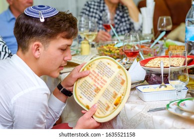 Jewish family celebrate Passover Seder reading the Haggadah. Young jewish boy with kippah reads the Passover Haggadah.