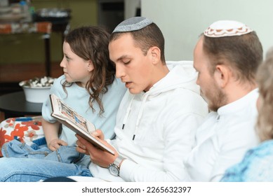 Jewish family celebrate Passover Seder reading the Haggadah. Young jewish man with kippah reads the Passover Haggadah. - Shutterstock ID 2265632397